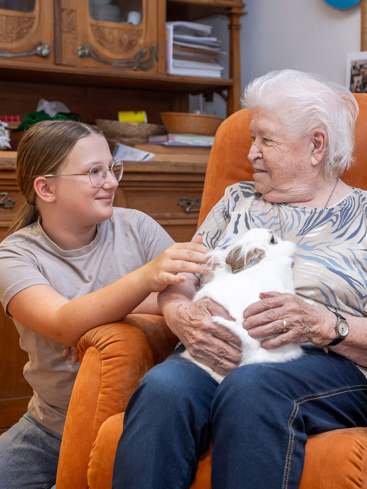 Ein Mädchen und eine alte Frau steicheln ein Kaninchen.