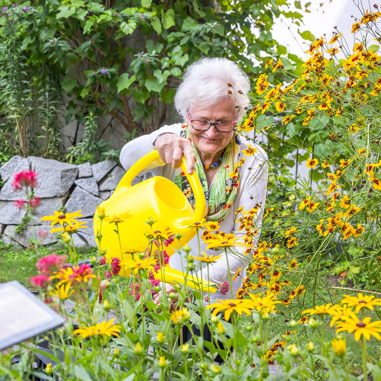 Eine alte Frau gießt Blumen im Garten.